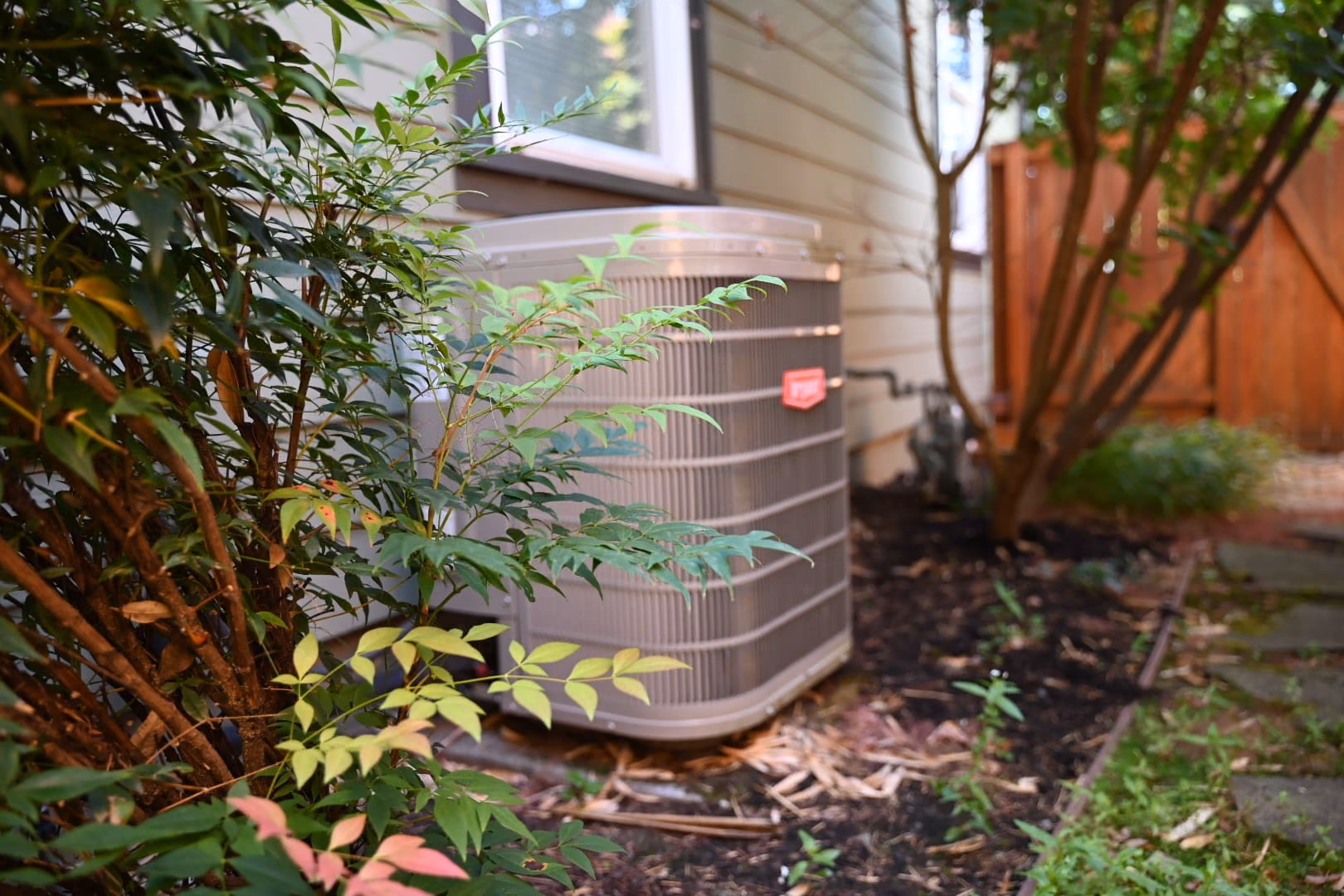 Outdoor air conditioner condenser installed beside a home with landscaping