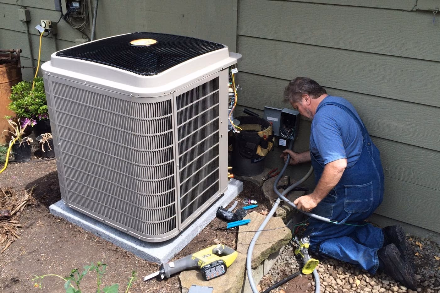 Technician in blue overalls installing a heat pump outdoor unit beside a home