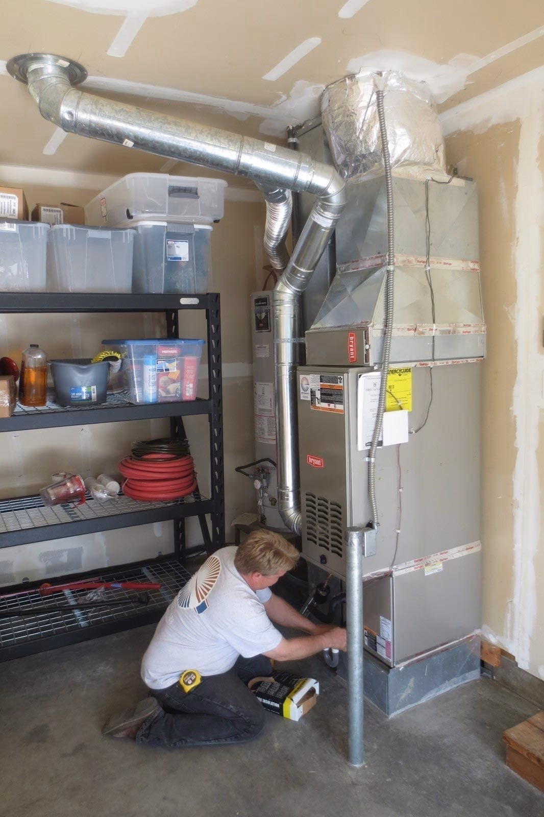Technician crouching beside a high efficiency gas furnace with silver ductwork